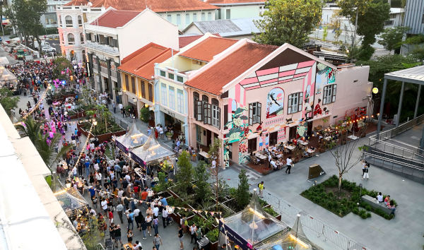 Street view of a crowded outdoor market in front of colorful buildings with red roofs.
